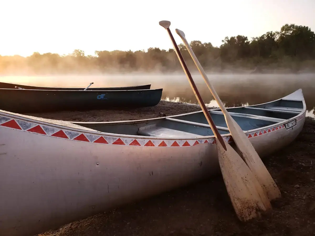 Canoes pulled up on a bank at dawn, mist rising off the water behind them