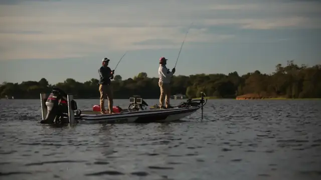 Two anglers casting from a bass boat on calm water at dusk