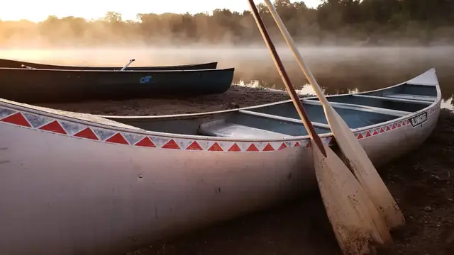 Canoes pulled up on a bank at dawn, mist rising off the water behind them