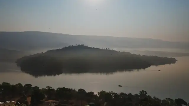 Fog over a wooded island in still water at sunrise