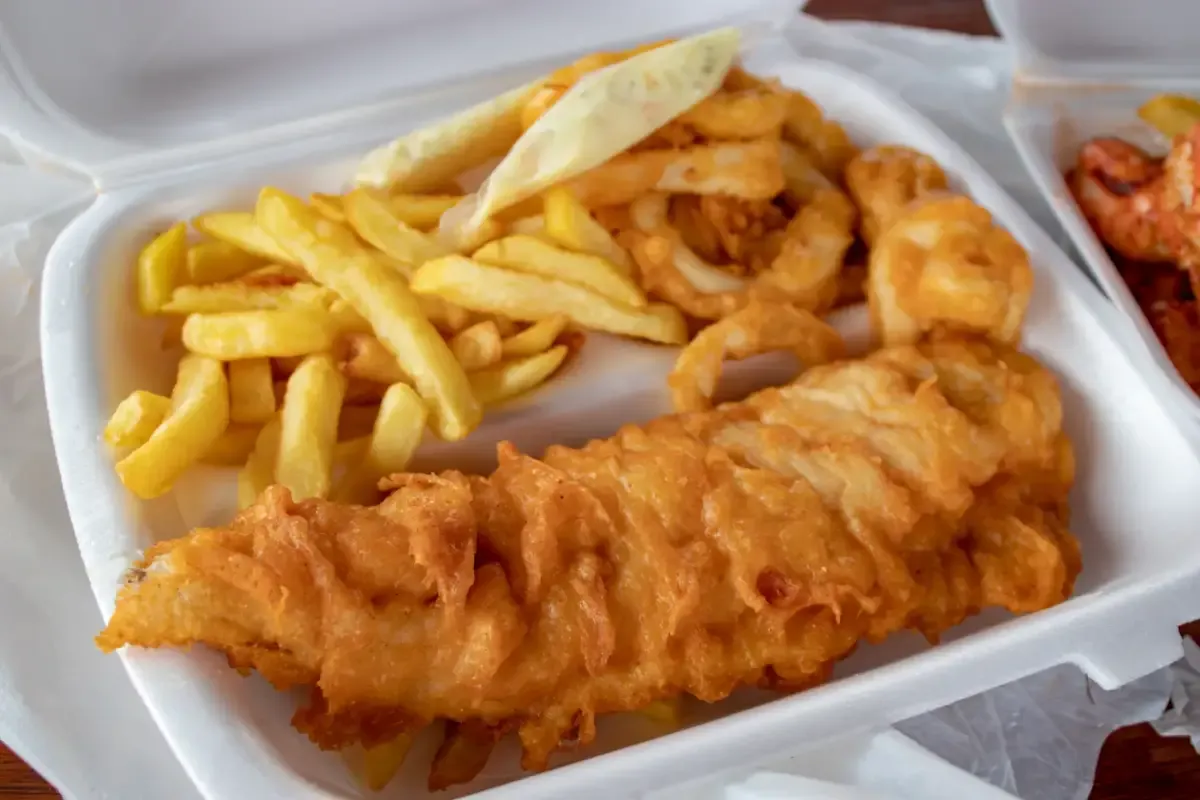 Battered fish, fries and onion rings in a carry-out container