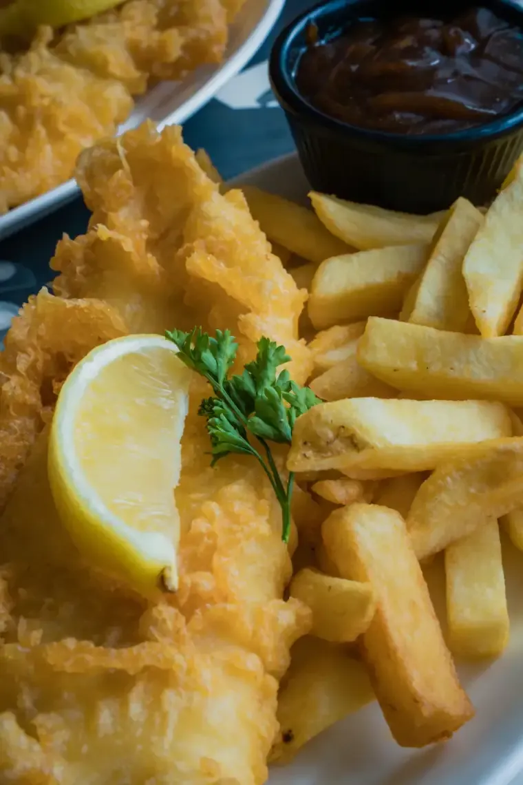 Two pieces of golden battered fish with fries, a lemon wedge and tartar sauce