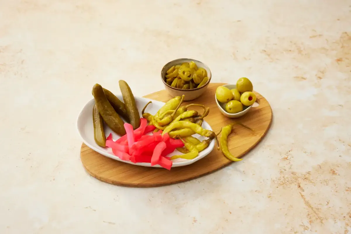 A relish tray of pickles, pickled peppers, olives and radish on a wooden board