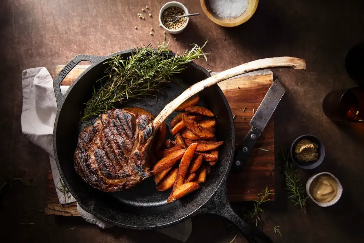 A seared bone-in steak in a cast-iron pan with roasted potato wedges and fresh rosemary