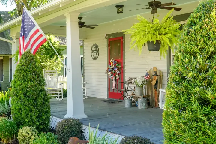 Covered front porch with white columns, hanging ferns, a flag and a red front door