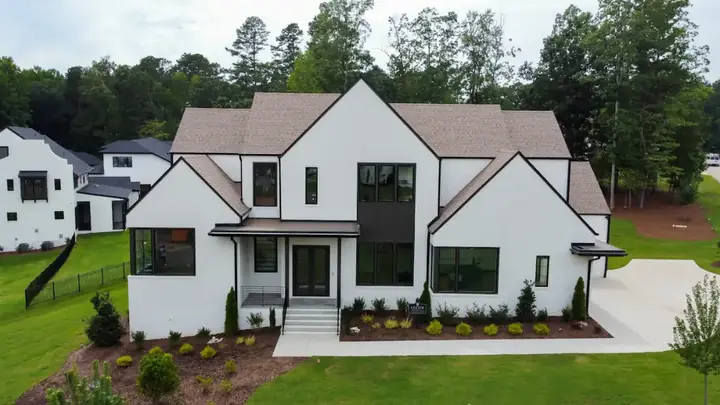 Large white farmhouse-style house with black windows and a gabled front, on a wide lawn