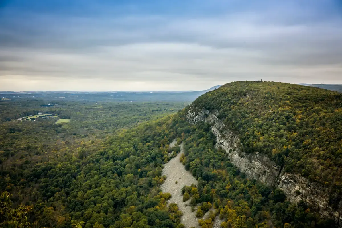 Green wooded bluffs and rock faces above a wide river valley, seen from the air under a gray sky