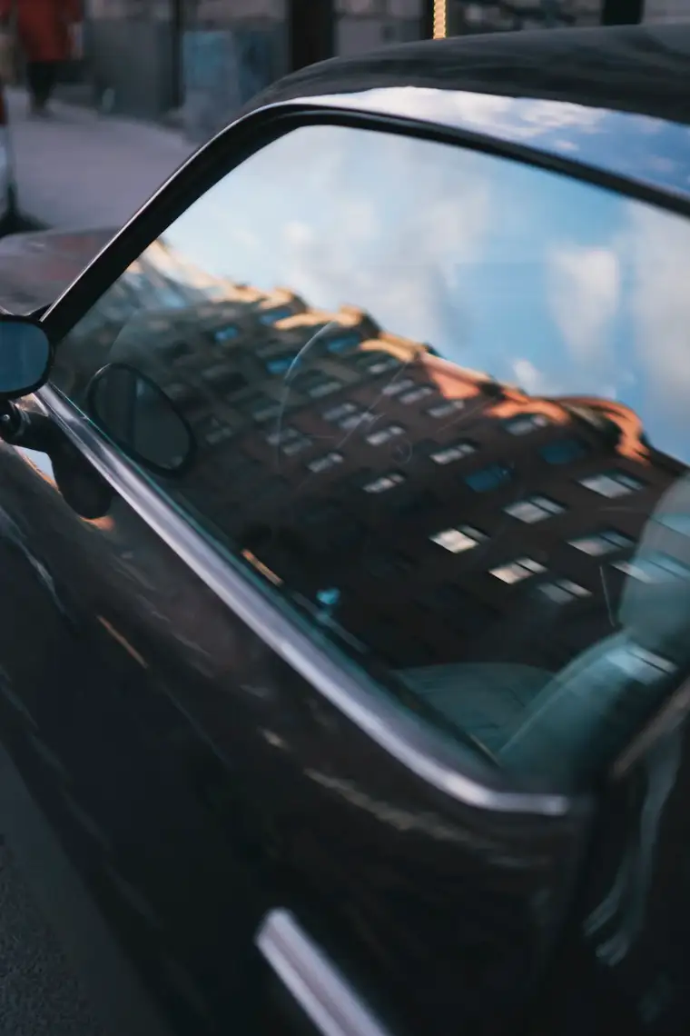 Black car door after polishing, so glossy it mirrors a brick apartment building and blue sky