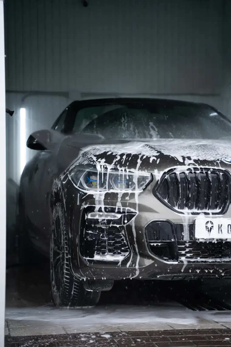A grey SUV in a wash bay with soap suds running down the hood and grille