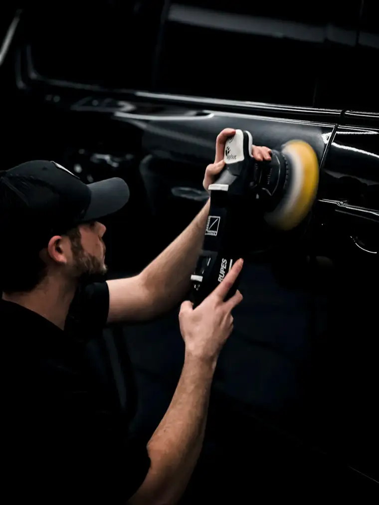 A detailer in a cap polishing a black car door with a yellow pad