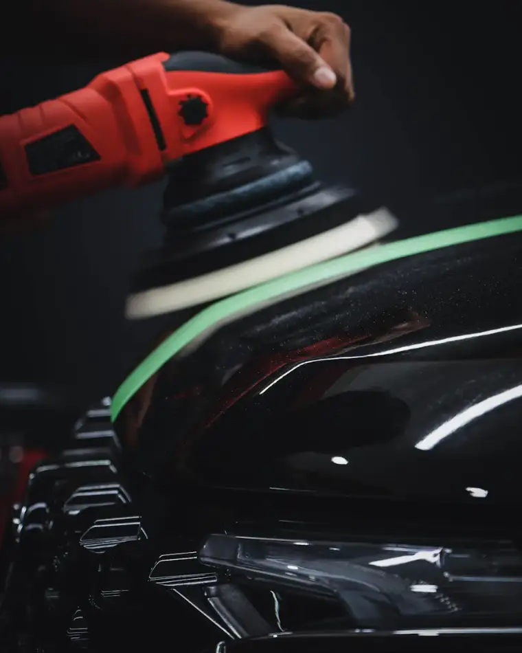 A red polisher working on black paint next to green masking tape