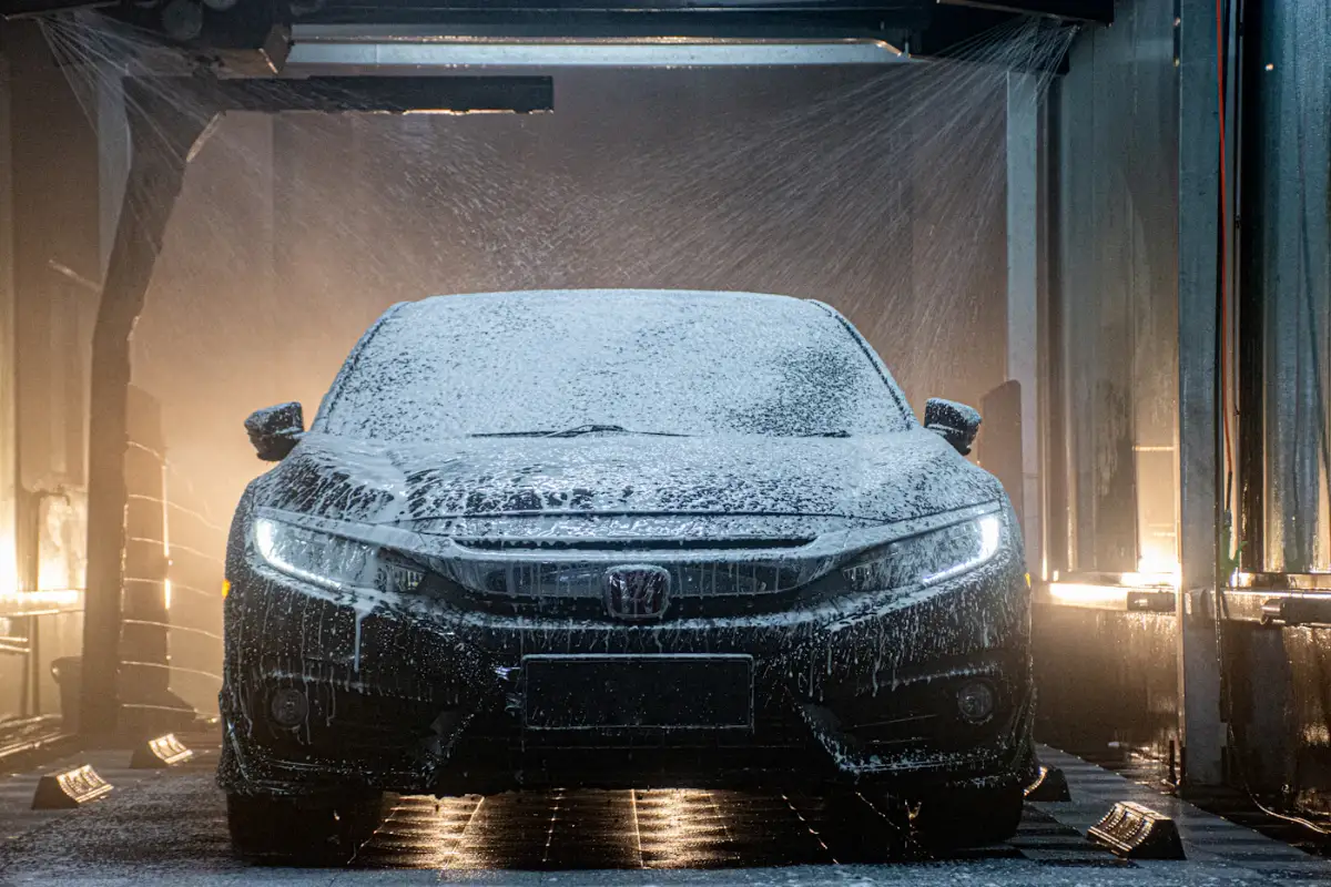 A sedan covered in foam inside a wash bay lit by warm lights