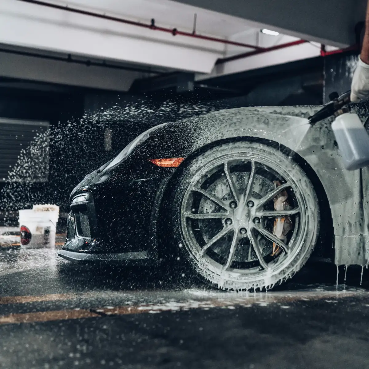 A foam cannon covering a black sports car wheel in thick foam