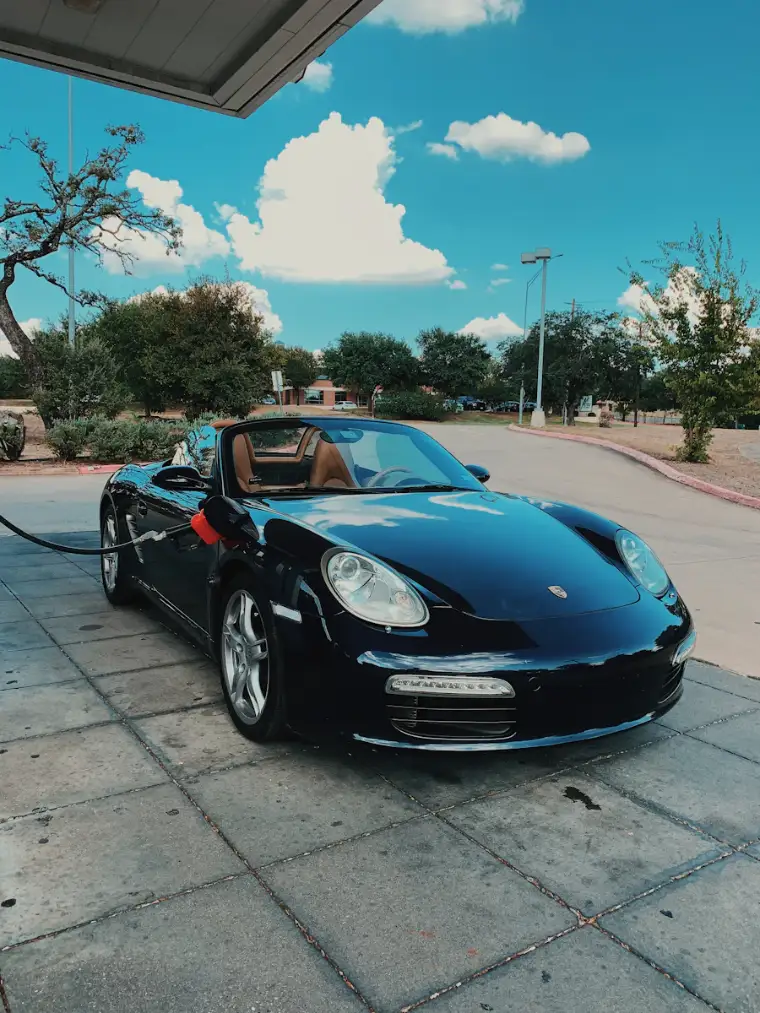 Dark blue convertible in the sun, paint reflecting clouds and trees