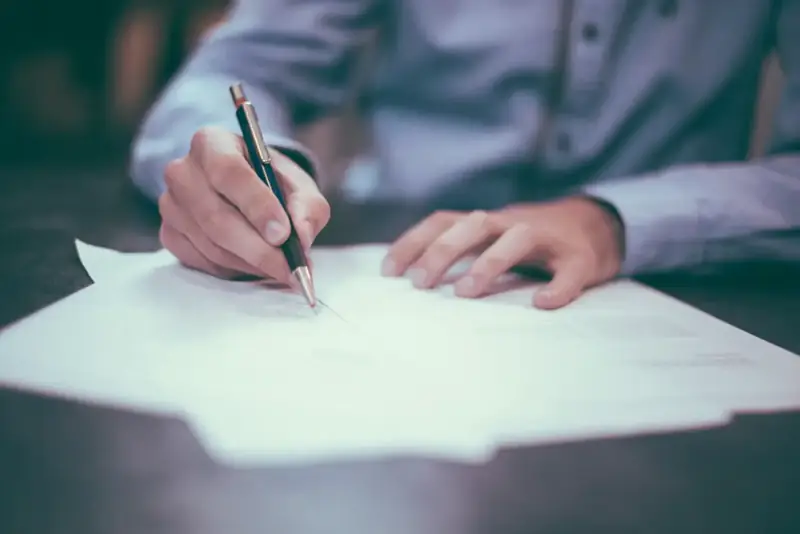 A person in a pale blue shirt signing a document with a fountain pen