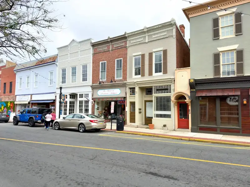 Two-story brick and clapboard storefronts along a quiet small-town main street on a sunny morning