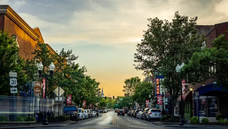 A small-town main street at sunset, with brick storefronts, street trees and parked cars