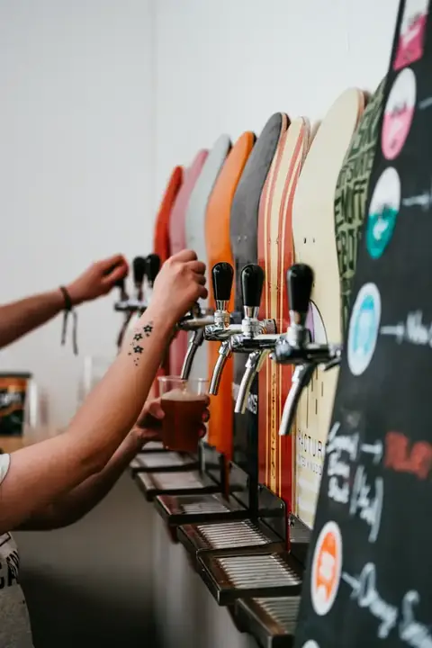 Hands pulling two beers at once from a wall of colourful tap handles