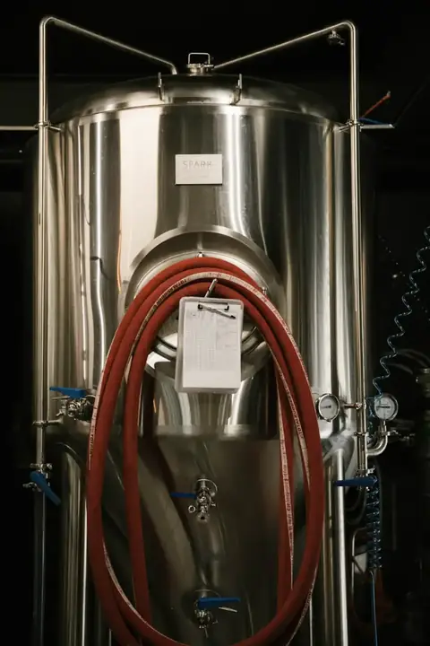 A steel fermenting tank with a red hose coiled on its side