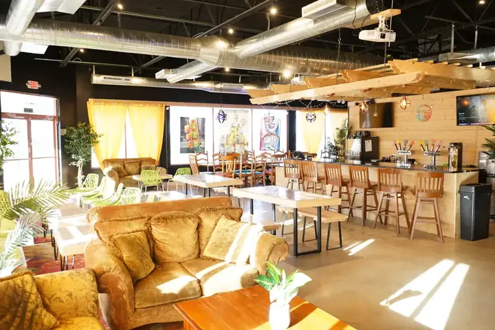 A bright taproom with leather armchairs by the window, long tables and a row of stools at the bar