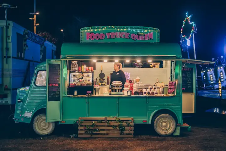A green food truck lit up at night with its serving window open