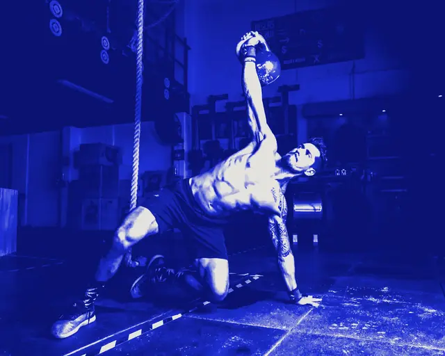 A man on one knee pressing a kettlebell overhead during a get-up.