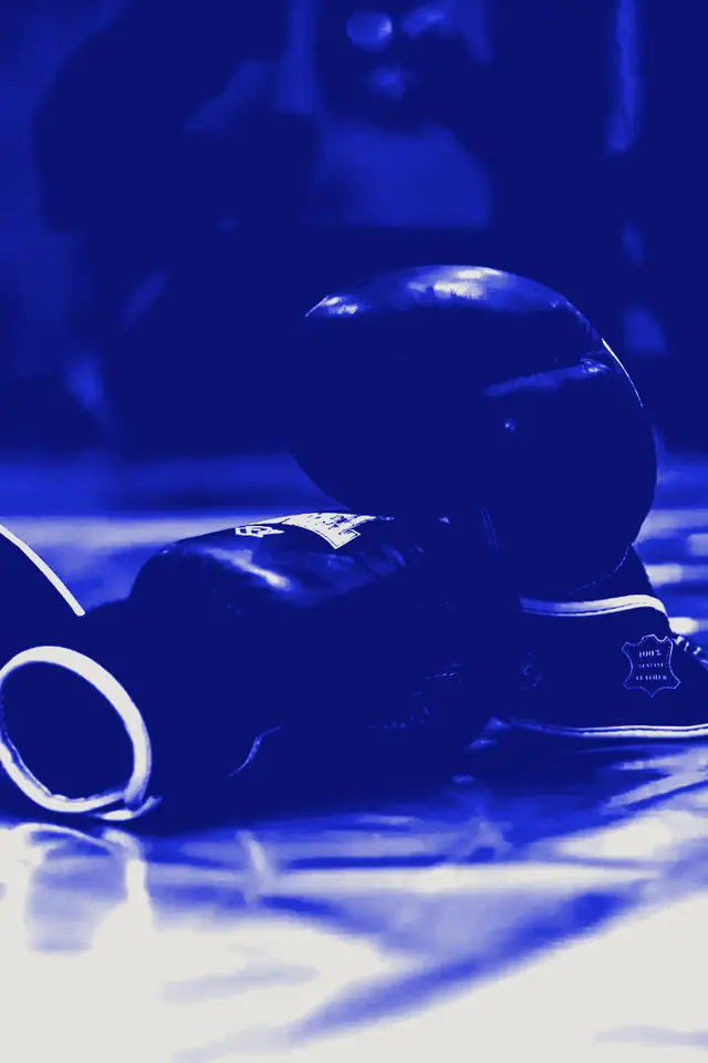 A pair of boxing gloves resting on a blue training mat.