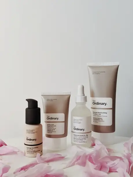 Four skincare bottles and tubes standing on pink flower petals