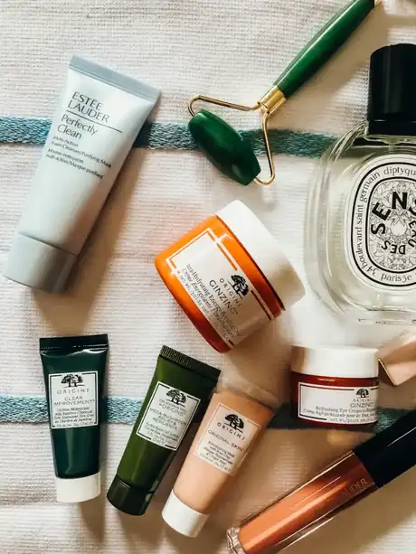 Skincare tubes, jars and a green jade roller laid out on a striped towel