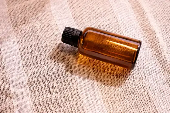 An amber serum bottle lying on soft pink linen