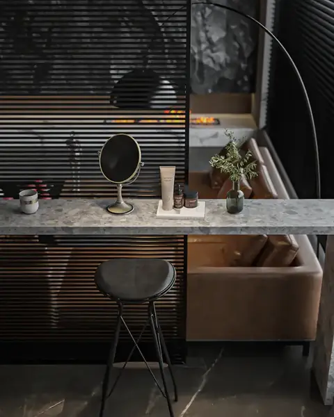 A quiet vanity corner with a round mirror, a marble counter, a stool and a low sofa