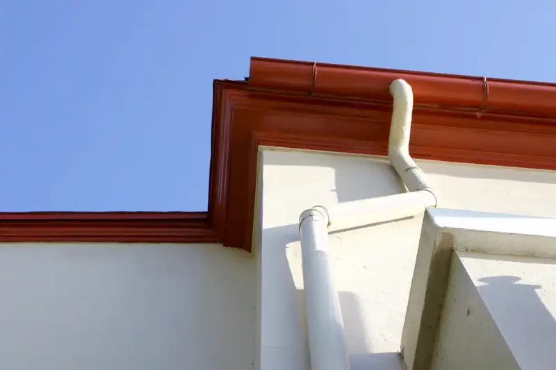A clean gutter with a white downspout turning down a white stucco corner
