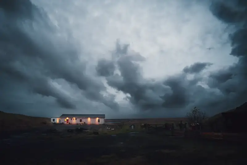 Dark storm clouds building over a lit farmhouse at dusk